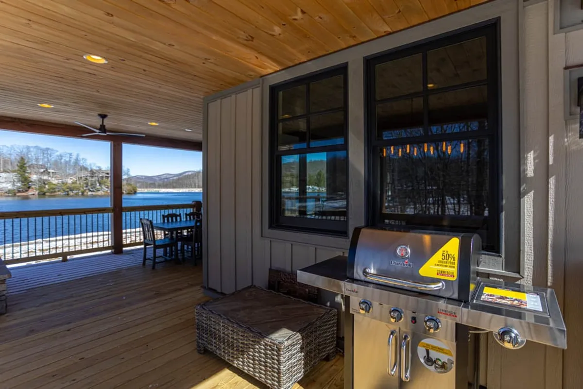 An exterior covered patio features a grill and comfortable seating, all facing a serene water view. The cheerful atmosphere suggests opportunities for barbecues, dining, and socializing, making it ideal for group get-togethers.