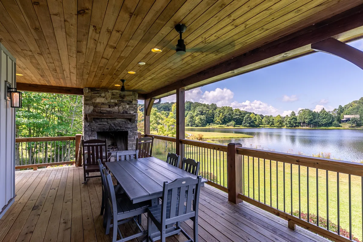 An inviting outdoor dining area set with a table and fireplace, framed by wooden beams and a stunning lake view. The setting is ideal for hosting friends or relaxing with family, and the fire pit suggests cozy evenings in a sophisticated environment.