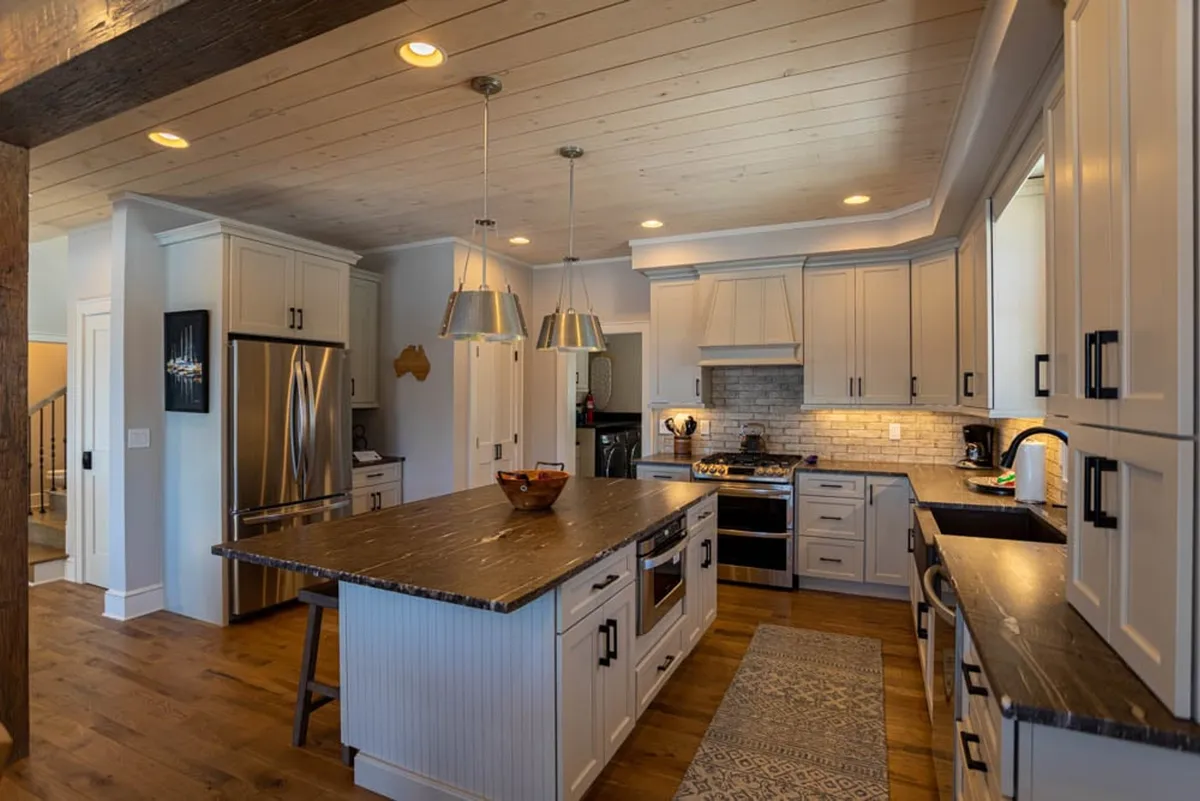 The kitchen’s central island features a rich, dark countertop, paired with stainless steel appliances and elegant pendant lighting. The setup is ideal for group cooking, casual breakfasts, or festive gatherings, capturing the kitchen's role as a social hub.